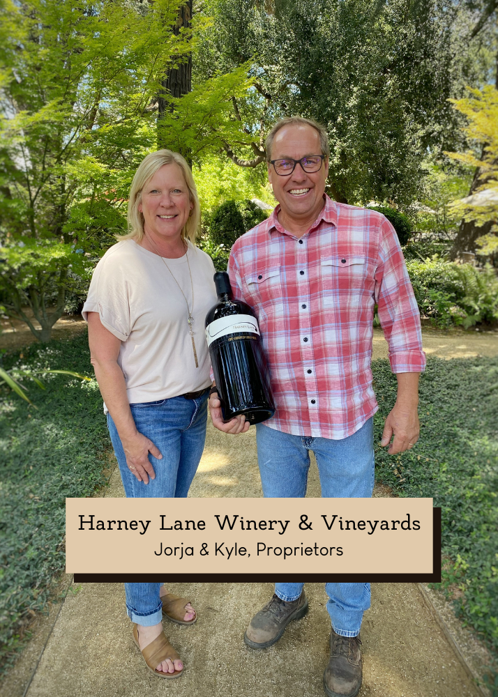 Jorja and Kyle, the proprietors of Harney Lane Winery and Vineyards, holding a giant bottle of wine in in the back garden area of their winery.